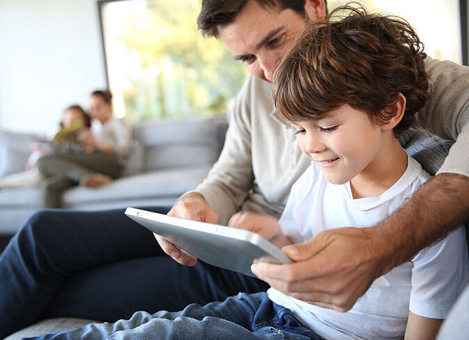 Ein Vater und sein Kind spielen gemeinsam mit einem Tablet.