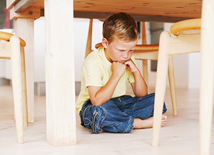 Wütender Junge sitzt unter Tisch