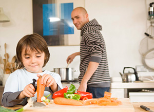 Vater guckt Kind in der Küche beim Karottenschälen zu